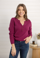 Woman wearing a purple waffle knit henley and blue jeans standing indoors.