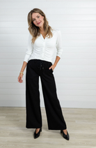 Woman wearing a white blouse and black pants against a plain background