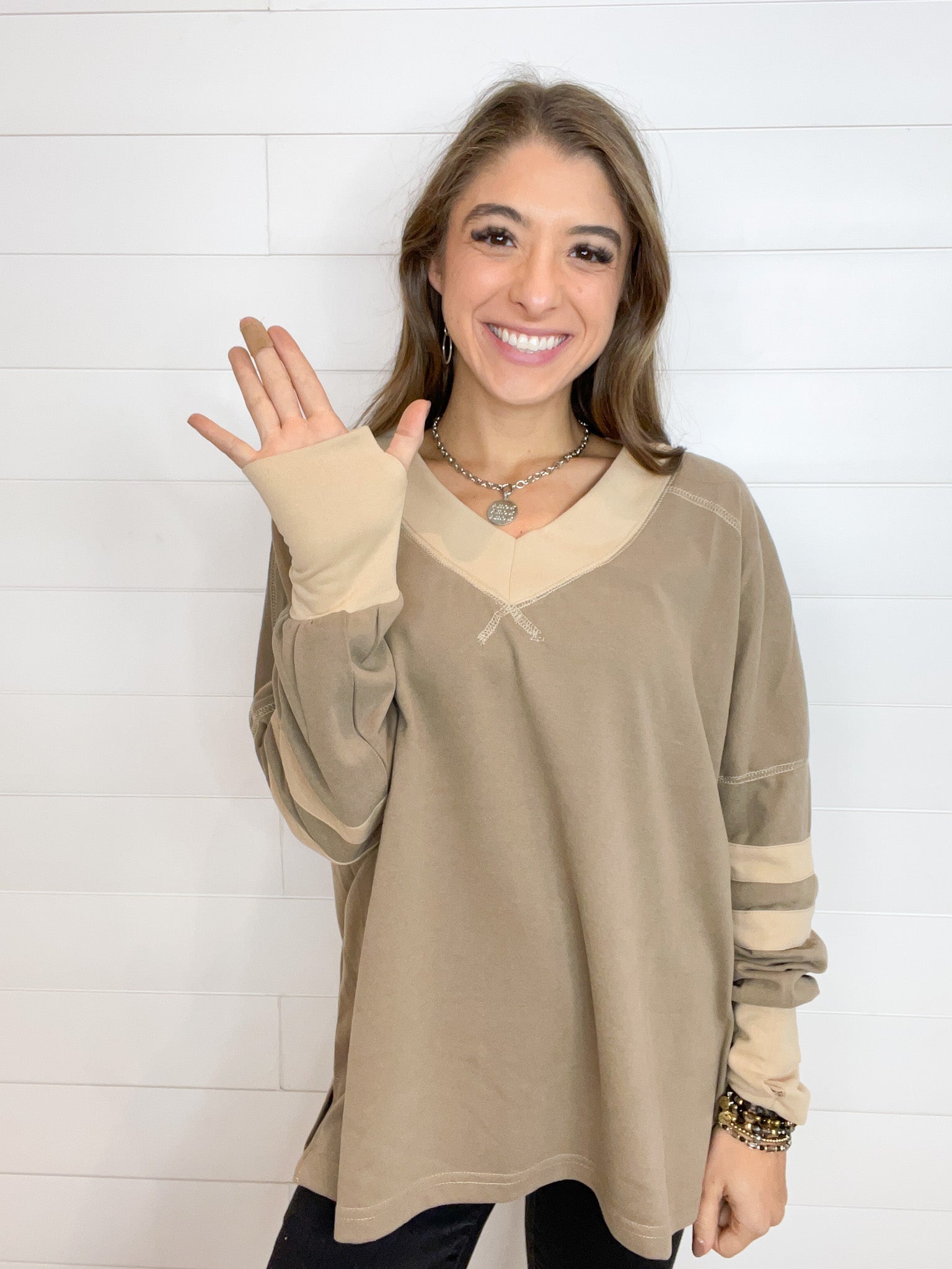 taupe long sleeve top with light tan section long v-neckline, drop shoulder, stripes low on the sleeves, and wide cuffs at the wrist featuring a thumbhole