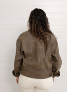 Person wearing a brown leather jacket from behind against a white wall