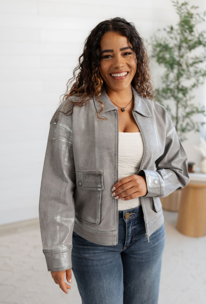 Woman wearing a gray jacket and blue jeans indoors with a plant in the background