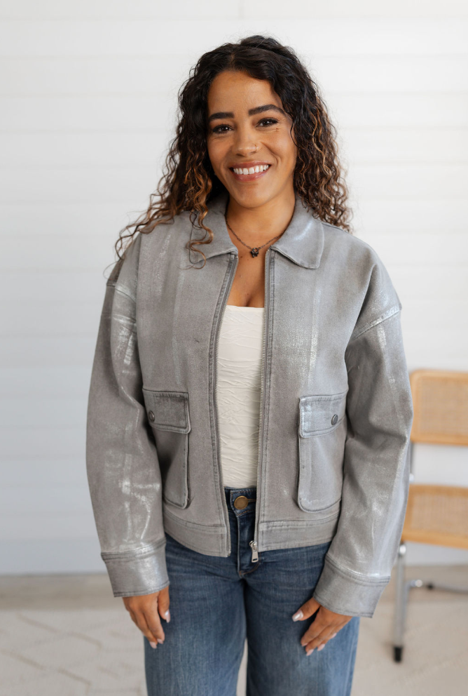 Woman wearing a gray jacket and blue jeans indoors with a white background