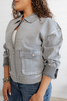 Person wearing a light, metallic gray denim jacket with rolled-up sleeves on a white background