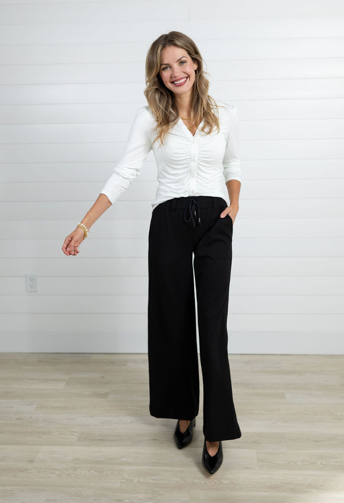Woman wearing a white blouse and black pants against a plain background