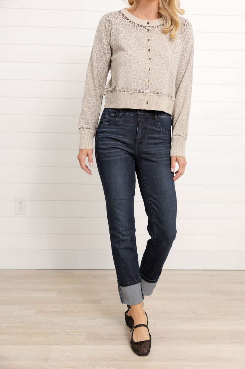 Woman wearing a beige patterned sweater and dark jeans against a white wall.