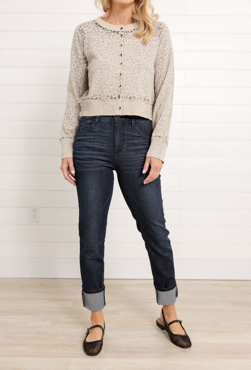 Woman wearing a beige patterned sweater and dark jeans against a white background